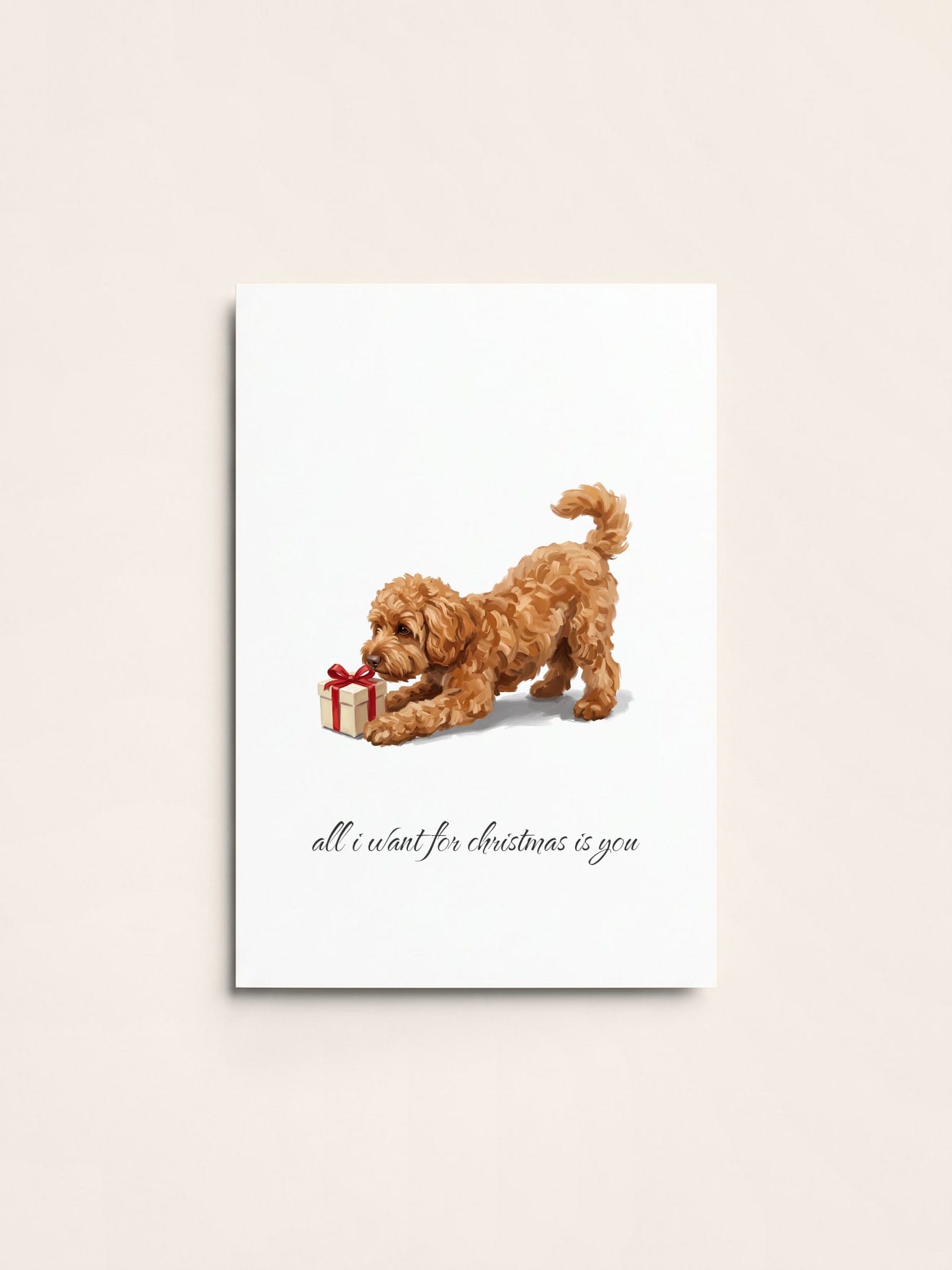 A Christmas card of an apricot cockapoo in a play bow, nosing at a wrapped present with a red bow